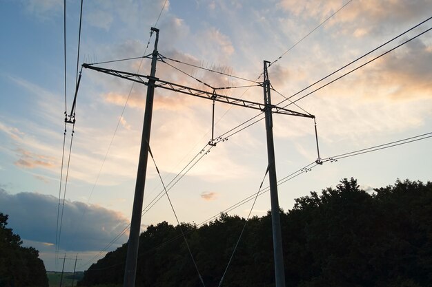 Silhouette sombre de la tour haute tension avec des lignes électriques au lever du soleil.