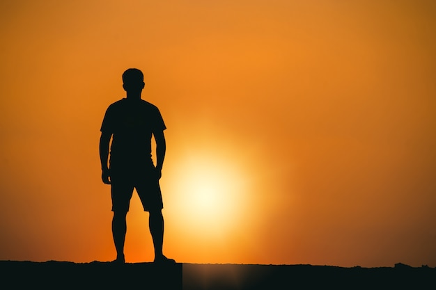 Silhouette de succès et de sérénité jeune homme debout sur un rocher dans les montagnes au coucher du soleil.