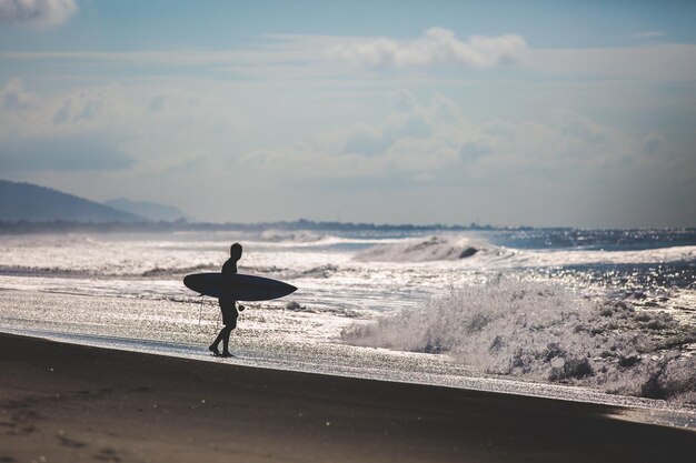 Photo silhouette d'un surfeur sur la plage contre le ciel