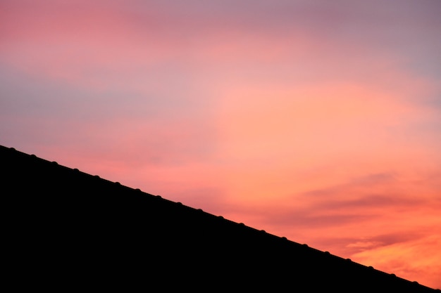 Silhouette de toit sur une nouvelle maison avec ciel de fantaisie rose avant fond de coucher de soleil