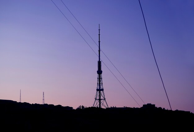 Silhouette de la tour de télécommunication avec des lignes électriques contre le ciel du matin