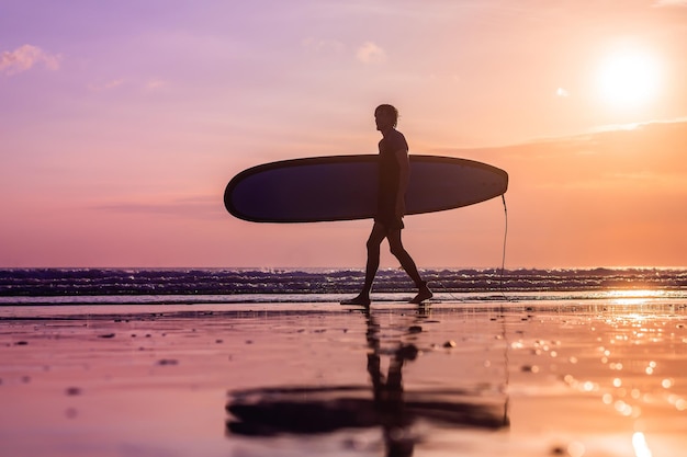 Silhouette de vacances d'un surfeur transportant sa planche de surf à la maison au coucher du soleil avec espace de copie