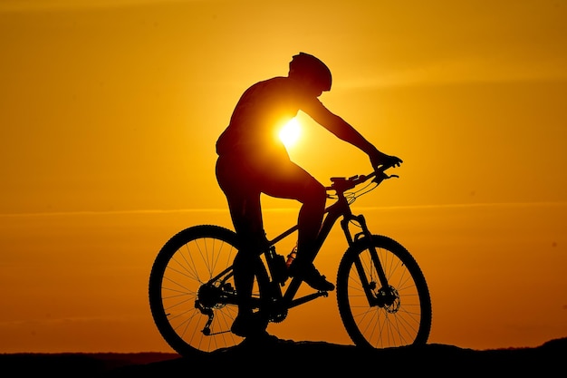 Silhouette d'un vélo sur fond de ciel au coucher du soleil au sommet d'une montagne