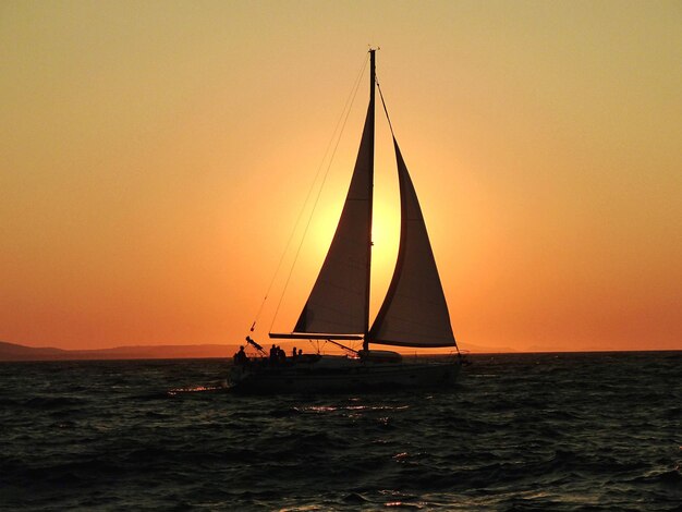 Silhouette d'un voilier qui navigue sur la mer contre un ciel clair au coucher du soleil