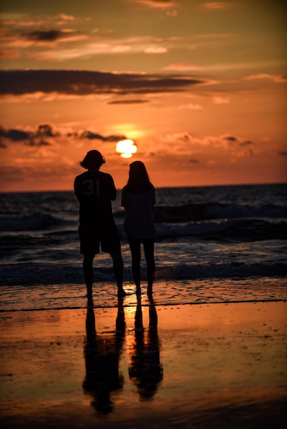 Des silhouettes d'amis debout contre la mer au coucher du soleil.