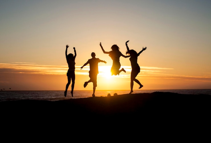 Photo des silhouettes d'amis sautant par la mer contre le ciel au coucher du soleil
