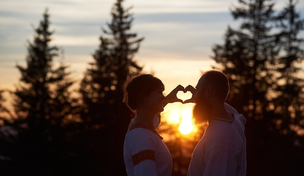 Silhouettes de couple amoureux au coucher du soleil gesticulant coeur