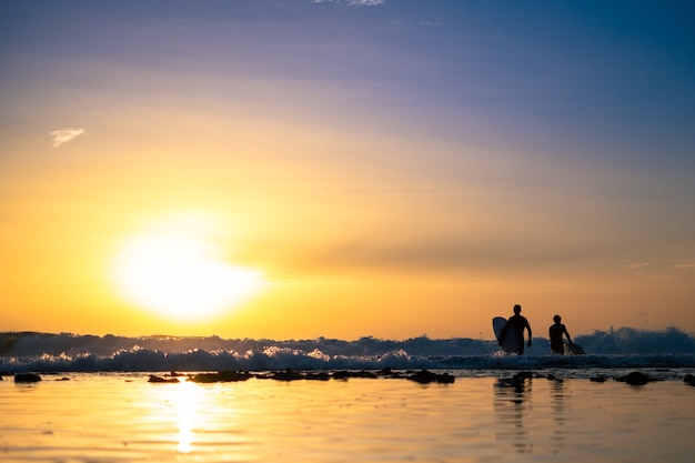 Silhouettes de deux hommes surfant au coucher du soleil