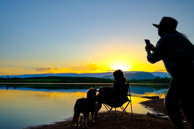 Silhouettes de deux jeunes femmes prenant une photo sur fond gris sur le lac à l'heure du coucher du soleil