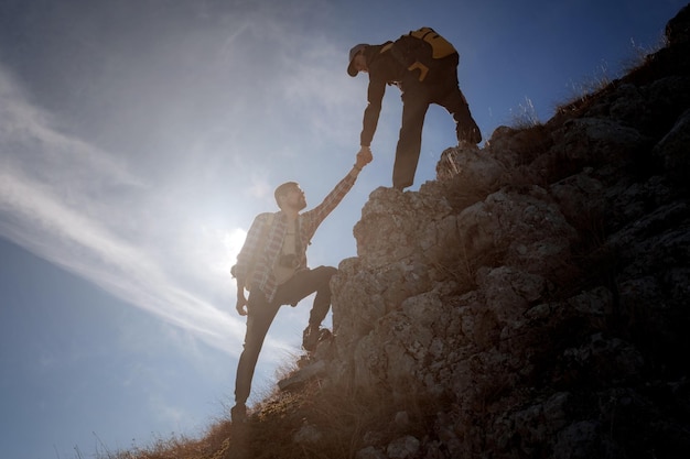 Silhouettes de deux personnes escaladant des montagnes et aidant contre le ciel bleu