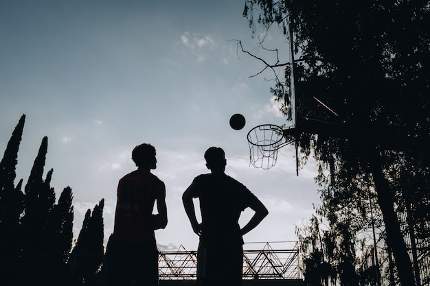 Silhouettes de deux personnes regardant un ballon de basket tomber dans le panier. basket-ball de streetball