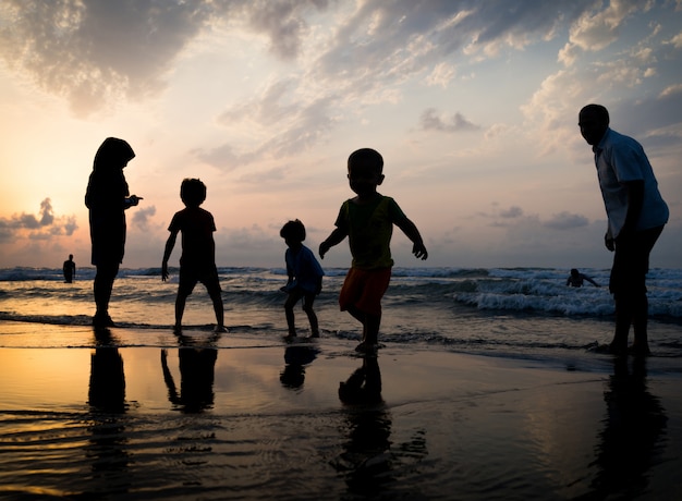 Silhouettes D'enfants Ayant Un Temps Heureux Sur La Plage De La Mer Près Du Coucher Du Soleil