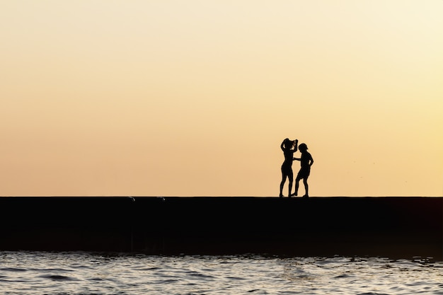 Silhouettes d'enfants debout sur la jetée de la mer.