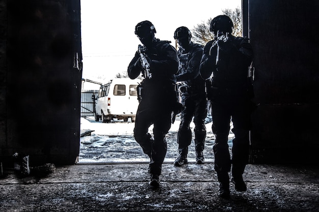 Photo silhouettes d'équipes tactiques des forces d'opérations spéciales de la police, combattants swat visant des fusils d'assaut tout en se tenant épaule contre épaule dans une porte d'un blanc éclatant. salle de prise d'assaut du groupe tactique militaire