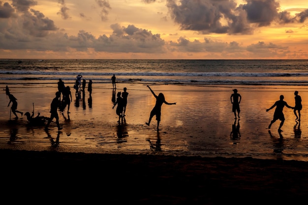 silhouettes de gars qui jouent au football au coucher du soleil sur la plage de l'océan.