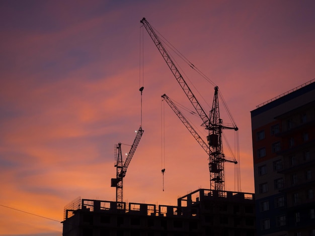 Silhouettes de grues à tour contre un ciel rouge du soir