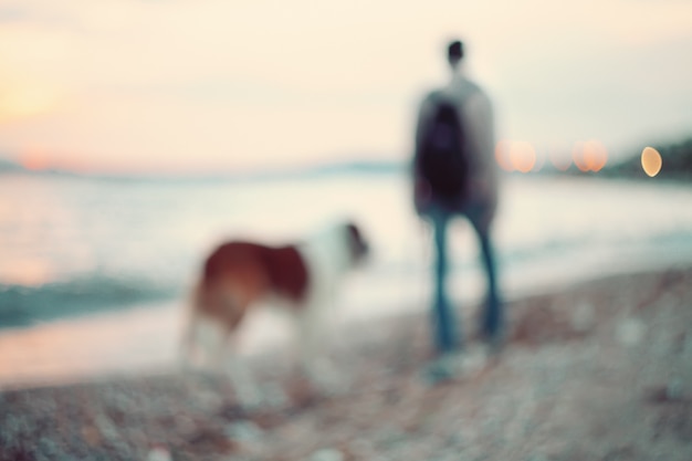 Silhouettes de l'homme et le chien marchant le long du bord de mer. Promenade nocturne au coucher du soleil.