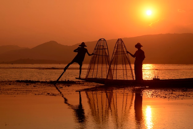 Silhouettes d'hommes pêchant dans le lac au coucher du soleil