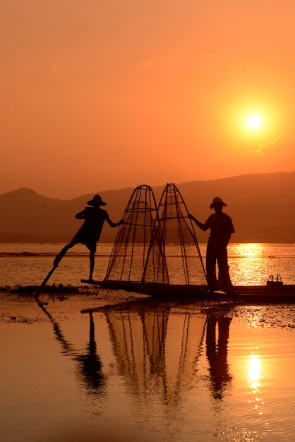 Silhouettes d'hommes pêchant dans le lac au coucher du soleil