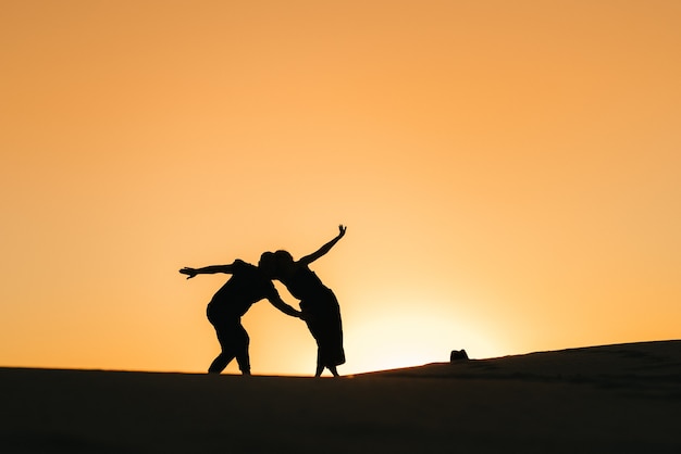 Silhouettes d'un jeune couple heureux et fille sur fond de coucher de soleil orange dans le désert de sable