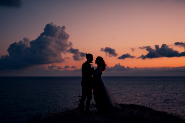 Silhouettes d'un jeune couple heureux et fille sur fond de coucher de soleil orange dans l'océan