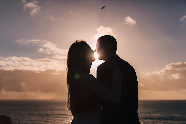 Silhouettes de jeunes mariés s'embrassant sur fond de coucher de soleil et d'océan