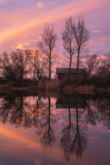 Silhouettes de maisons et d'arbres d'un village abandonné sur le lac contre un écarlate lumineux, coucher de soleil d'automne.