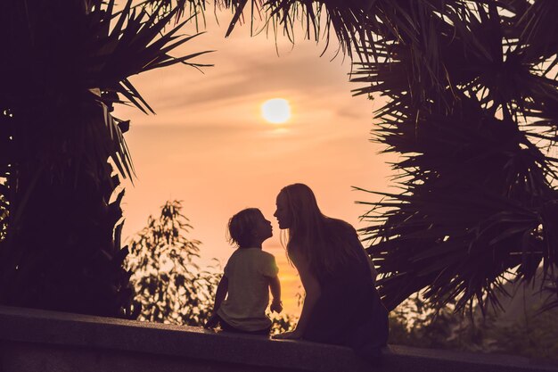 Silhouettes de mère et de fils, qui rencontrent le coucher de soleil sous les tropiques sur fond de palmiers