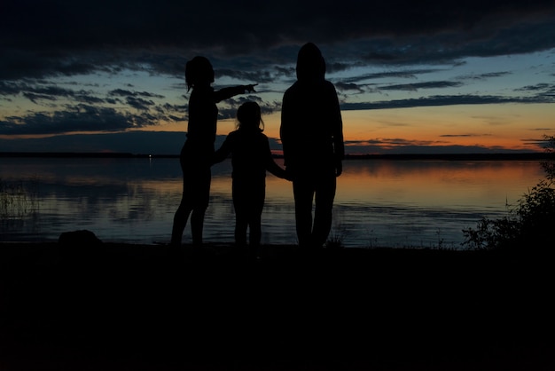Silhouettes de mères et d'enfants regardant le coucher de soleil sur le lac. Concept de famille