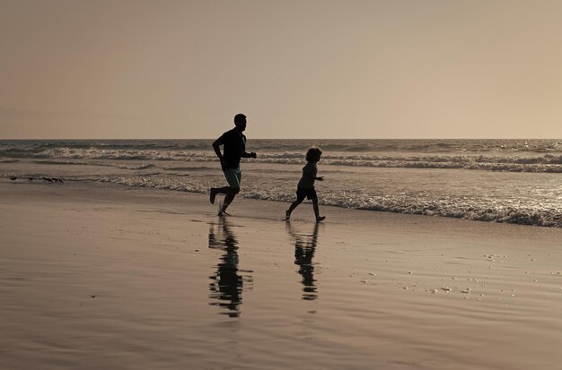 Silhouettes père et fils courant s'amusant et ressentant la liberté sur l'enfance de plage d'été