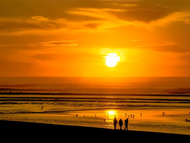 Photo des silhouettes de personnes marchant sur la plage contre le ciel au coucher du soleil