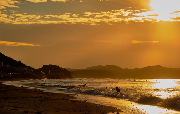 Photo des silhouettes de personnes sur la plage contre un ciel orange au lever du soleil