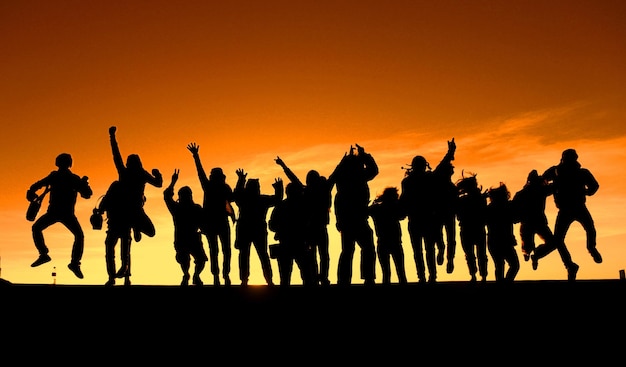 Des silhouettes de personnes sautant sur le terrain au coucher du soleil