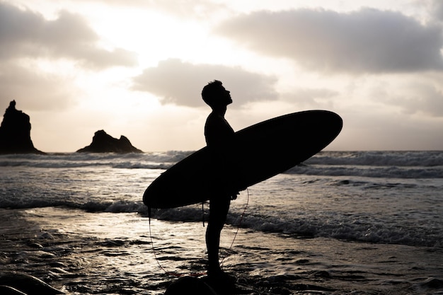 Photo silhuoette d'un surfeur à la plage pendant le coucher du soleil en regardant le ciel