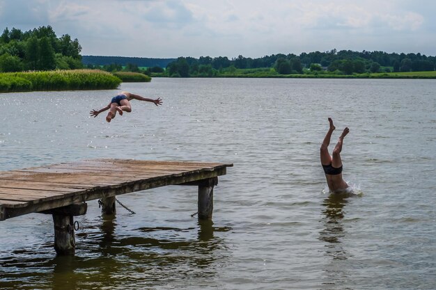 Sillhouette d'hommes plongent dans l'eau du lac près de la jetée en bois