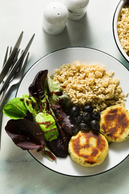 Un simple déjeuner ou dîner végétalien pour une famille de deux adultes et un enfant riz brun avec okara de soja et galettes de pommes de terre avec salade fraîche et olives sur une table en marbre