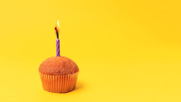 Un simple gâteau éponge sans crème avec une bougie de vacances brûlante sur fond jaune avec un espace de copie.