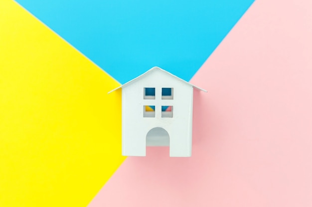 Simplement concevoir avec maison miniature jouet blanc isolé sur bleu jaune rose pastel coloré tableau géométrique tendance concept de maison de rêve d'assurance de biens hypothécaires. Espace de copie plat vue de dessus.