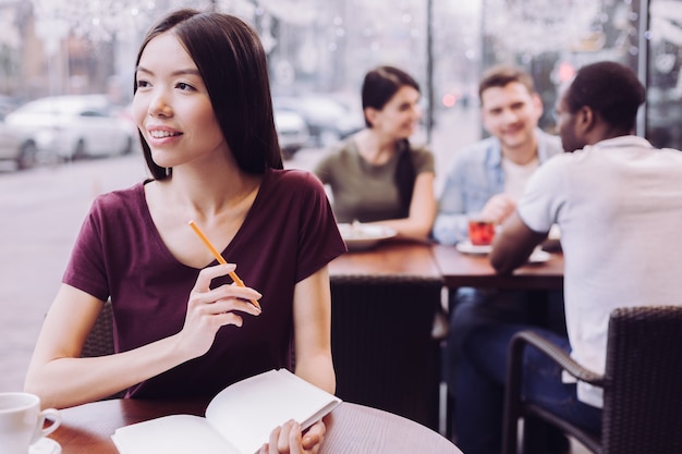 Sincère belle étudiante regardant de côté et portant un crayon tout en planifiant l'exécution des tâches