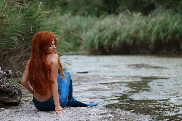 une sirène dans un costume bleu avec de longs cheveux roux dans la rivière