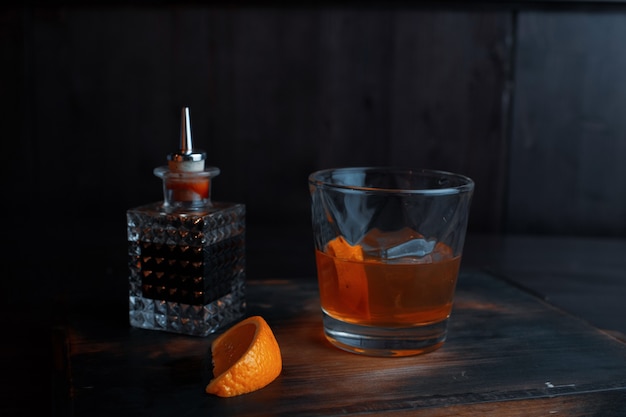 Sirop alcoolisé sucré dans un gobelet en cristal se dresse sur une table dans un pub à côté d'une bouteille en cristal. La boisson est décorée de tranches d'orange.