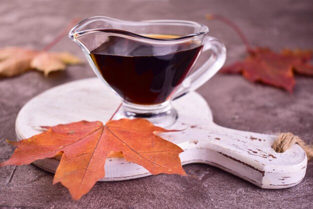 Photo sirop d'érable dans une saucière transparente sur fond de feuilles d'érable