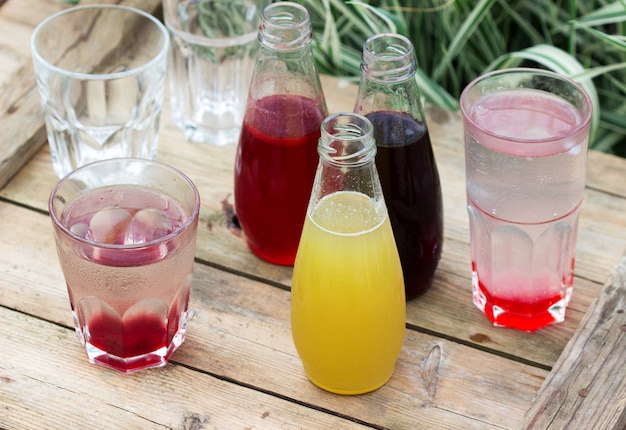 Sirops De Fraise, Cerise Et Rhubarbe Et Verres Avec De L'eau Sur Une Table En Bois Dans Le Jardin.