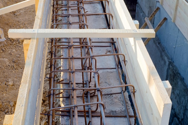 Site de fondation de nouveaux détails de construction et renforts avec des barres d'acier et du fil machine dans une terrasse en bois se préparant au coulage du ciment