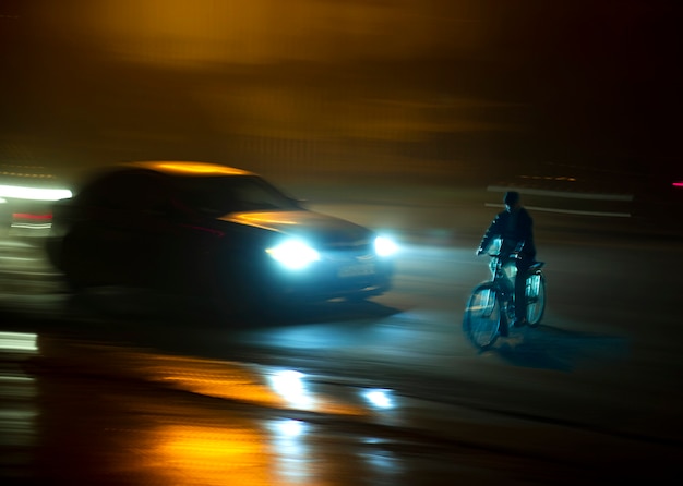 Situation dangereuse de la circulation urbaine avec cycliste et voiture dans la ville la nuit en flou de mouvement