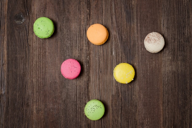 Six macarons multicolores sur une table en bois marron. Vue de dessus