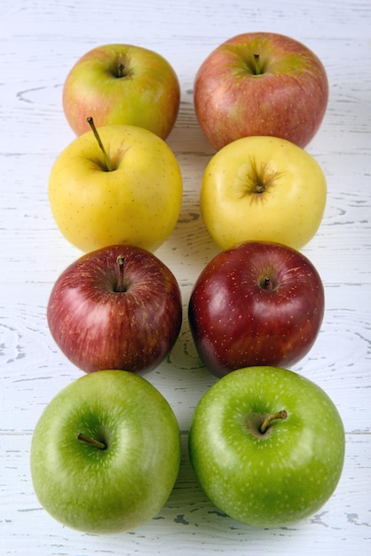 Six pommes multicolores sur un fond en bois blanc.