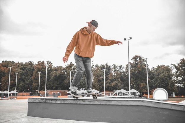 Skate, équilibre. Guy in cap sweatshirt et jeans sur skateboard regardant attentivement vers le bas en glissant sur un piédestal poussant avec le pied