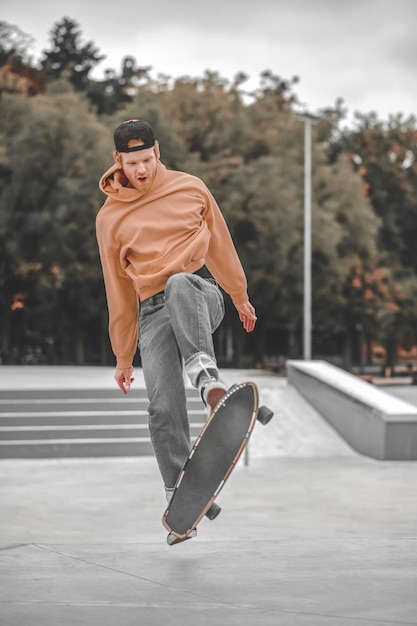 Skateboard, truc. Mec roux optimiste en casquette avec skateboard effectuant un tour de saut dans un skatepark