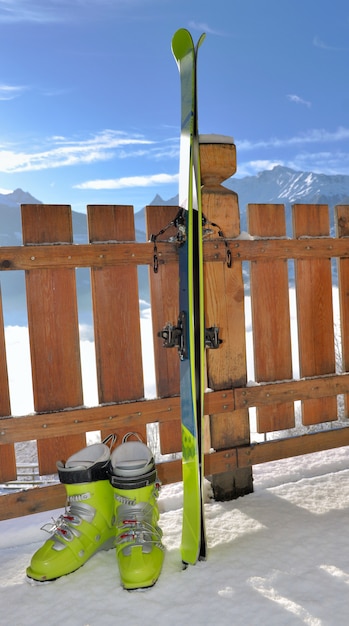 Ski de randonnée et chaussures contre une clôture en bois d'une terrasse enneigée avec vue sur la montagne